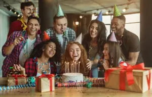 Friends celebrating around a birthday cake with party hats and gifts